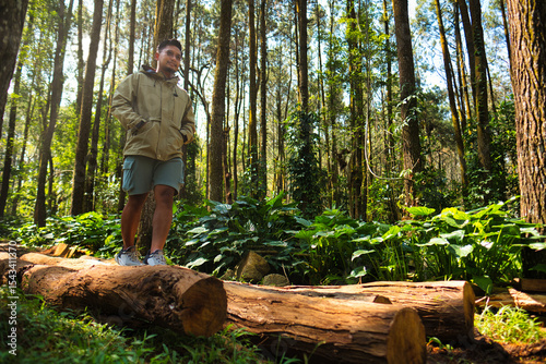 Man Walking on Forest Log Surrounded by Tall Trees and Lush Greenery