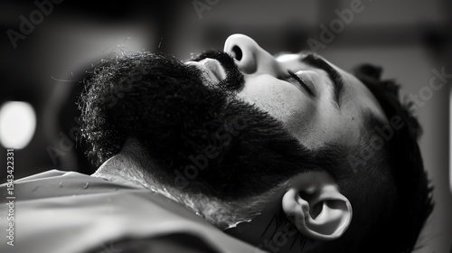 A black and white close-up photo of a man getting his beard trimmed. The man is relaxed with his eyes closed.