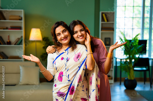 Smiling Indian mother and daughter looking at camera indoors with positive expressions