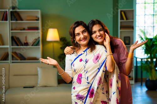 Smiling Indian mother and daughter looking at camera indoors with positive expressions