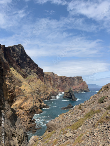 Vertical photo of small bay on island of Madeira, high rocky coastline, and ocean waves crashing on large rocks.