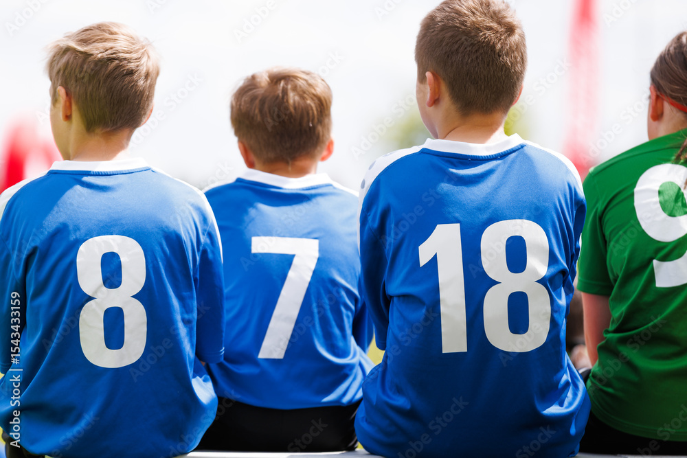 Fototapeta premium Young Soccer Players in Blue Jerseys Sitting on a Bench. Kids Play Sports in Summer Day. Youth Football Competition