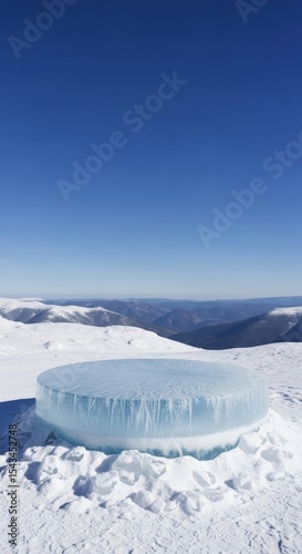 A large, round ice sculpture rests atop a snow covered mountain landscape under a blue sky
