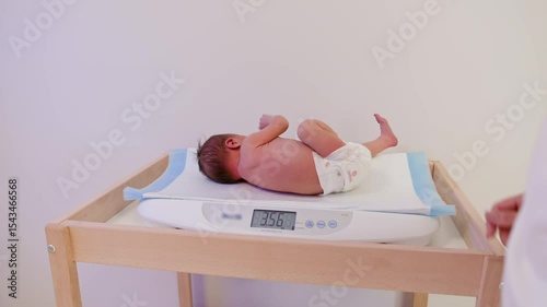 Newborn baby lying on a scale in a clinic, potentially undergoing medical observation or examination.