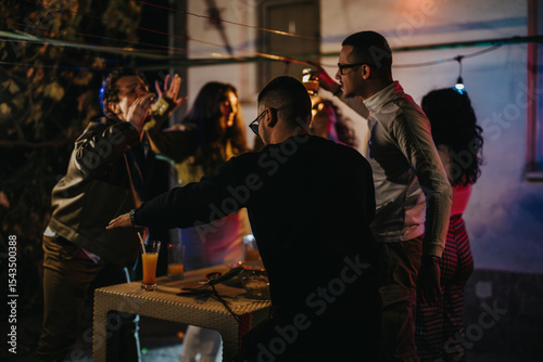 Obraz na płótnie A group of friends celebrate in a vibrant outdoor setting at night, enjoying drinks, conversations, and music under string lights