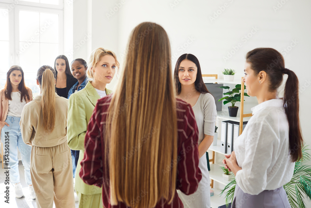 Obraz premium Group of diverse women standing together in bright room, talking and smiling during casual meeting. Females interacting and exchanging ideas, fostering teamwork and support in friendly atmosphere.