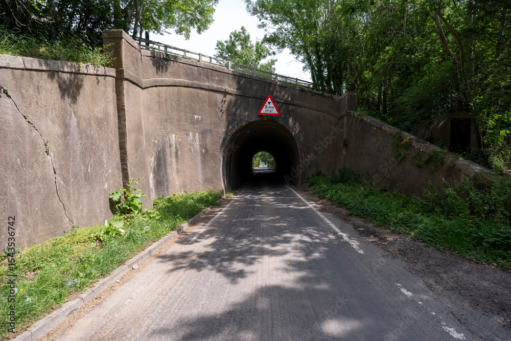 Obraz premium Narrow road passing under a low bridge in the english countryside