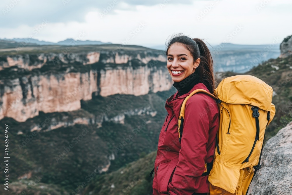 Naklejka premium Smiling woman with a backpack stands on a mountaintop overlooking a canyon.