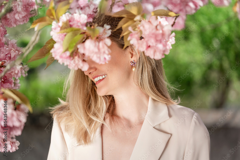 Fototapeta premium Elegant woman posing with blooming blossoms in spring. Elegant pearl and gemstone jewelry, smiling and enjoying a warm spring day.