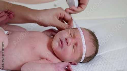 A doctor measuring a newborn's head circumference in a clinic setting. The baby appears to be receiving medical care, possibly neonatal phototherapy.