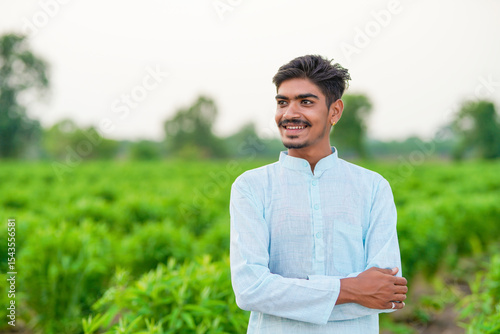 young indian farmer standing at green agricultural field