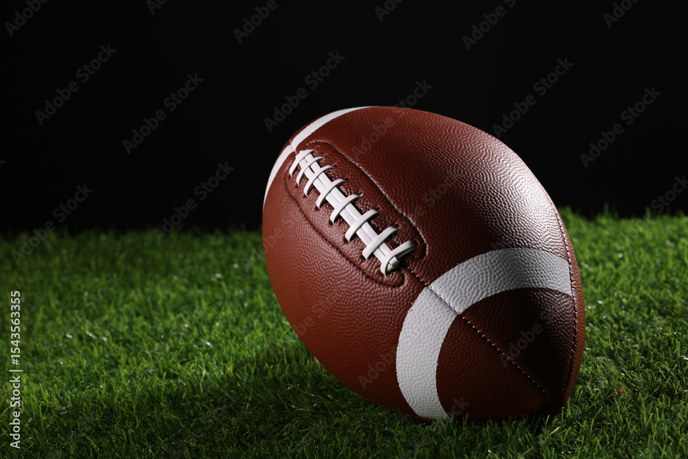 A textured American football resting on the green artificial turf with white line. College Football A textured American football resting on the green artificial turf with white line. College Football
