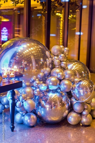 A collection of metallic silver and chrome-coloured spheres and balloons of varying sizes, reflecting colourful lights on a floor.
