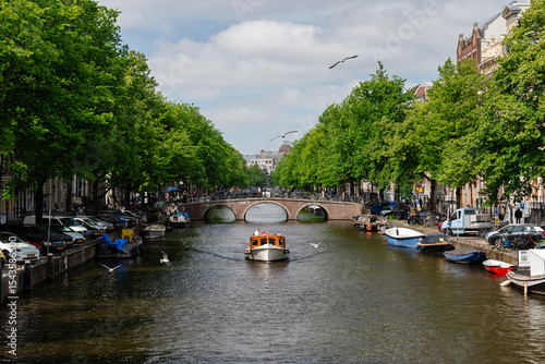 Amsterdam, Netherlands – May 21, 2025: Private boat cruising Amsterdam canal under brick arch bridge