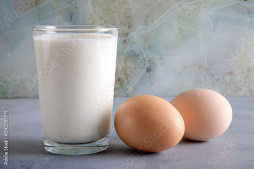 Glass of milk and two eggs on blue table,front view