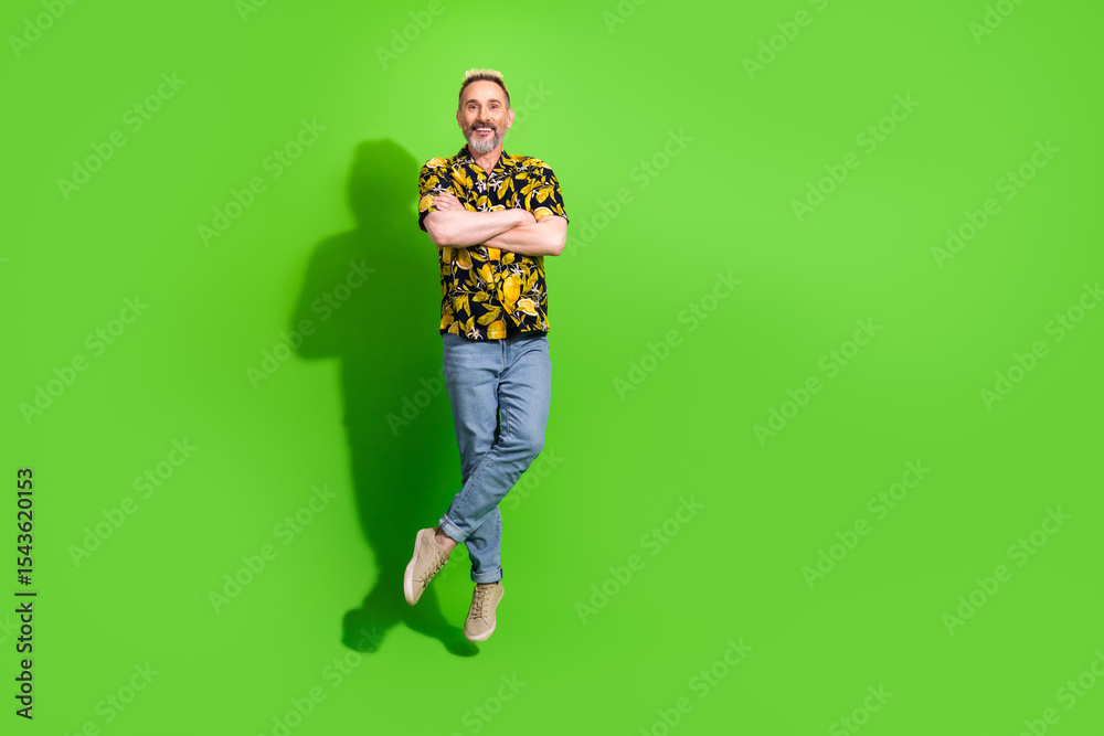 Fototapeta premium Cheerful middle aged man in a vibrant summer shirt posing against a solid green background, exuding fun and style