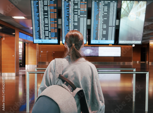 A young female traveler checks the airport departure board wearing a backpack. Concept of travel planning and journey anticipation, navigating in airport..