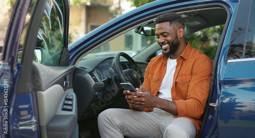 Smiling african american man sits in his car looking at his phone