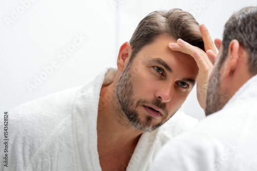 Close-up portrait of perfect brunet man touching chin and skin. Handsome man touching face in front of the mirror in bath. Perfect skin. Man cosmetic, skin treatment. Hygiene and skin care male face.