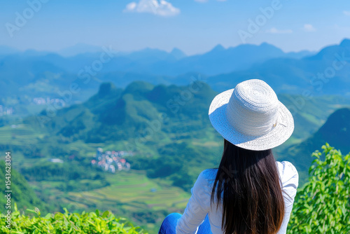 Serene landscape view featuring woman wearing wide brimmed hat, gazing lush green mountains and valleys. scene captures