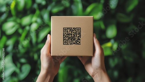 Hands Holding Square Cardboard Box Featuring Black QR Code Against Lush Greenery Background