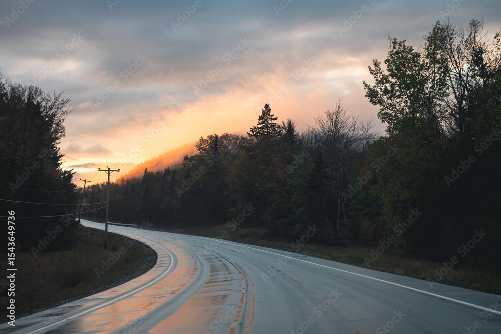Fototapeta premium view of a curved road in a mountainous area with a wet surface under a sunset sky