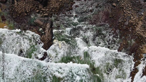 Top-down aerial view of ocean waves crashing onto the sand at Praia da Amália, Costa Vicentina, Portugal. Captured in slow motion, showing a dramatic coastal scene.
