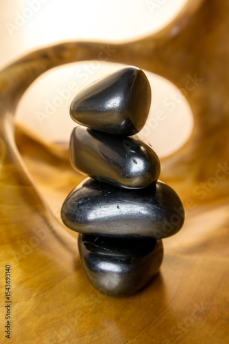 Stack of black stones on a wooden surface. The stones are arranged in a pyramid shape, with the largest one at the bottom and the smallest one at the top