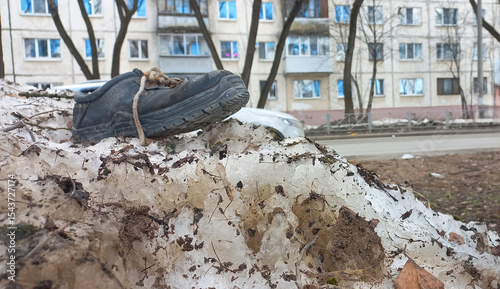 Black torn boot on dirty snow pile in urban environment