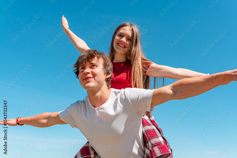 A young couple teenagers, a girl and a boy outdoor, laughing and smiling, Piggyback ride with open arms in the form of an airplane, the concept of freedom A young couple teenagers, a girl and a boy outdoor, laughing and smiling, Piggyback ride with open arms in the form of an airplane, the concept of freedom