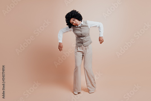 Confident businesswoman in stylish formal wear posing against a beige background showing a unique hand gesture.