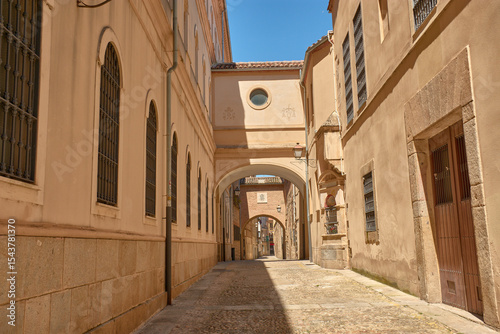 Encarnacion Street in Plasencia, Extremadura, a medieval passageway with arches and historic buildings basking in the sun.