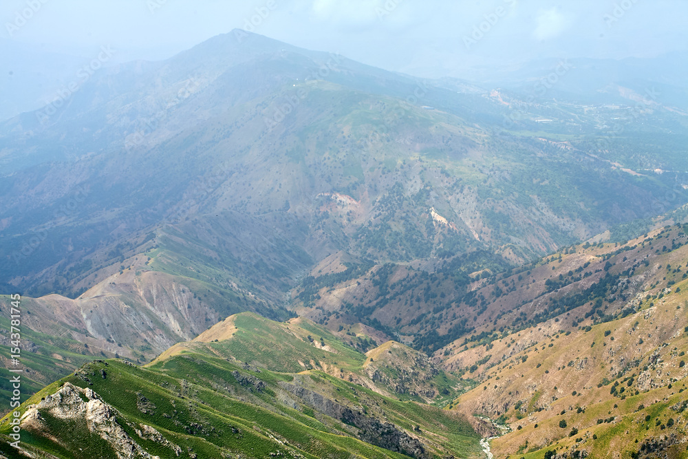 Obraz premium Majestic mountain landscape. Sharp ridges, partly in mist. From rugged rocks to green slopes. The wild nature of Tashkent Region, Uzbekistan