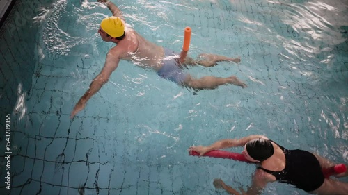 Professional swimming instructor guides a student using a floatation device in an indoor pool, providing support and encouragement during a lesson