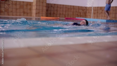 Professional female swimmer performing precise backstroke technique, executing rhythmic arm strokes with graceful body motion in crystal clear swimming pool water