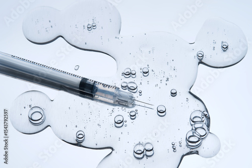 Fotografía A syringe with a needle and the texture of a cosmetic product with bubbles on a blue background