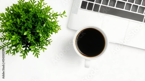 A cup of coffee rests beside a laptop and small plant on a white desk.