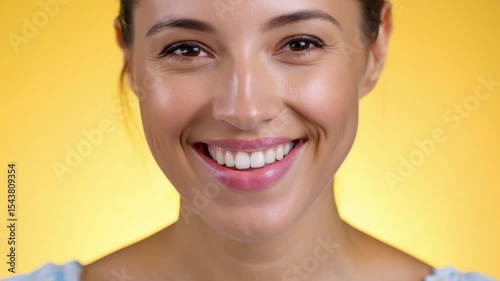 Close-up view of a smiling young Caucasian woman on a yellow background. The cheerful woman embodies warmth and joy, creating an inviting scene with the yellow backdrop.