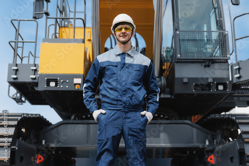 Portrait young man Mining industry worker standing confidently in front of heavy machinery crawler excavator