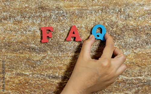 Hand Arranging FAQ Letters Against a Textured Background