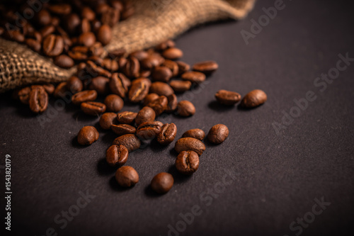 Rich, dark roasted coffee beans spread across a black surface next to burlap fabric, evoking the essence of freshly brewed coffee