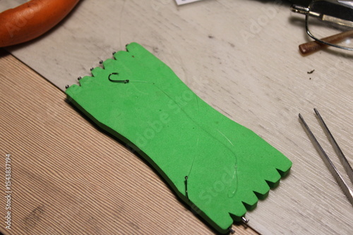 A green plastic fishing line winder with multiple fishing hooks attached. Commonly used by anglers to store and organize fishing lines and tackle. 