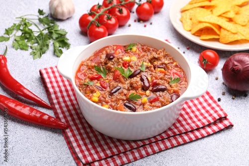 Photos Tasty chili con carne in bowl, nachos and ingredients on grey table, closeup