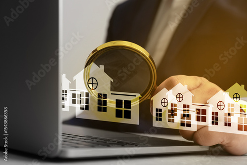 Real estate agent looking at buildings icons with magnifying glass over laptop, closeup. Search for housing photo