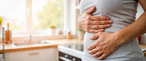 Hand gripping abdomen in kitchen, expressing discomfort and concern