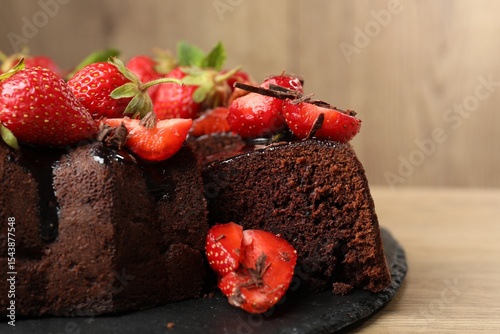 Delicious chocolate bundt cake with strawberries on wooden table, closeup photo