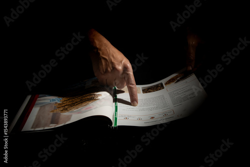 Primer plano de una mano humana señalando un libro de recetas en fondo oscuro con iluminación puntual que resalta el gesto de lectura
