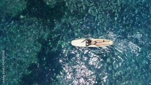 Surfer woman on surfboard in blue ocean. Attractive surf girl swims on longboard. Drone view