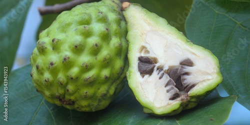 A fresh cherimoya fruit, cut open to reveal its seeds and pulp, sits on a leaf.