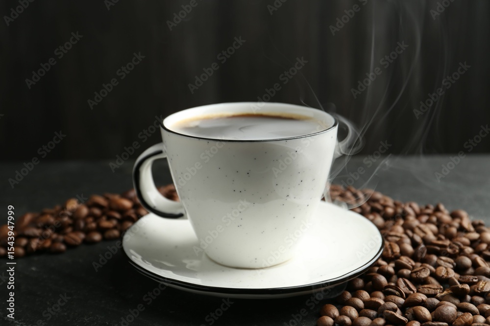 Fototapeta premium Aromatic coffee in cup and beans on black table, closeup